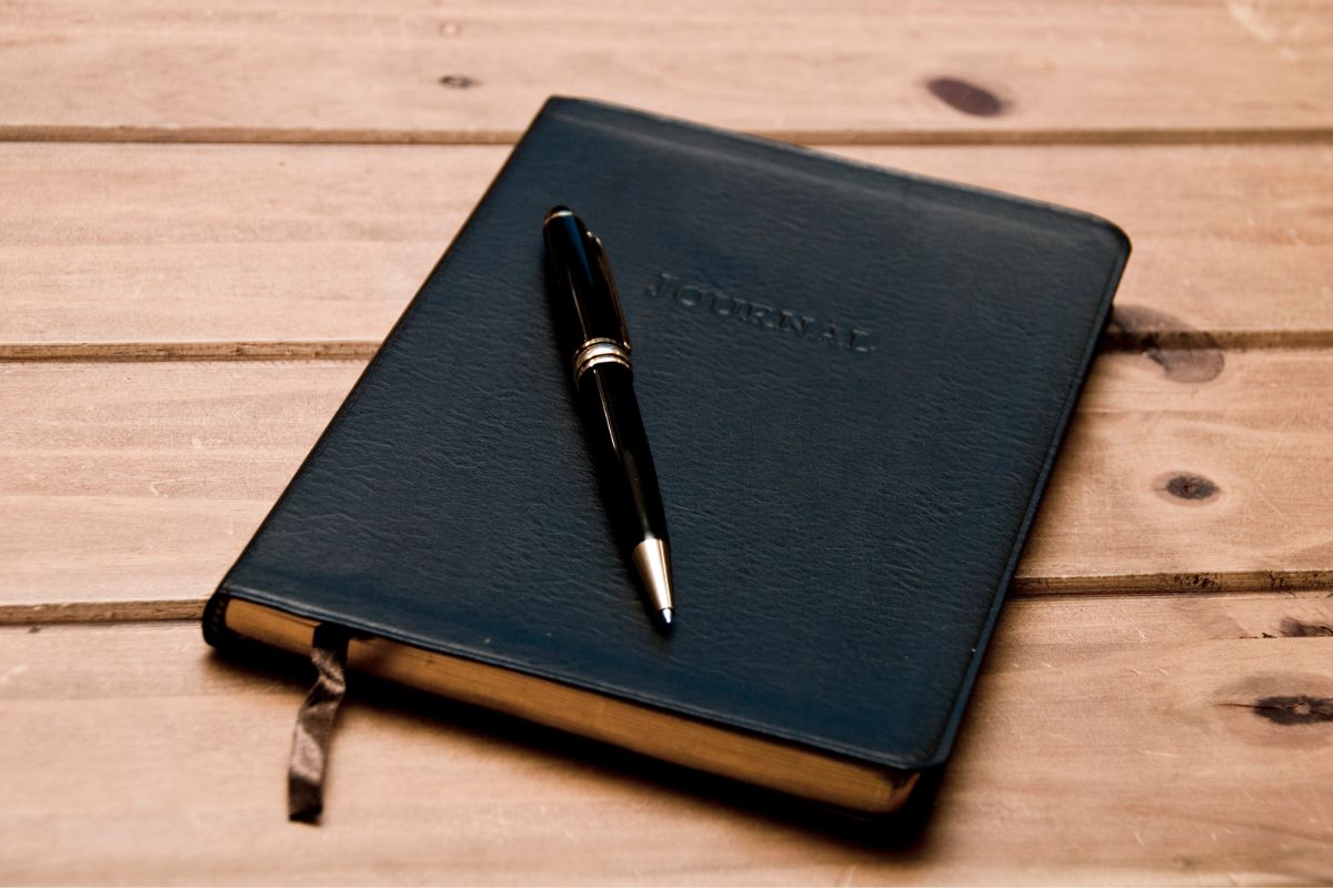 The image shows a notebook and a pen which means starting a financial wins journal is one of the simplest ways to stay on track and build a stable financial future.