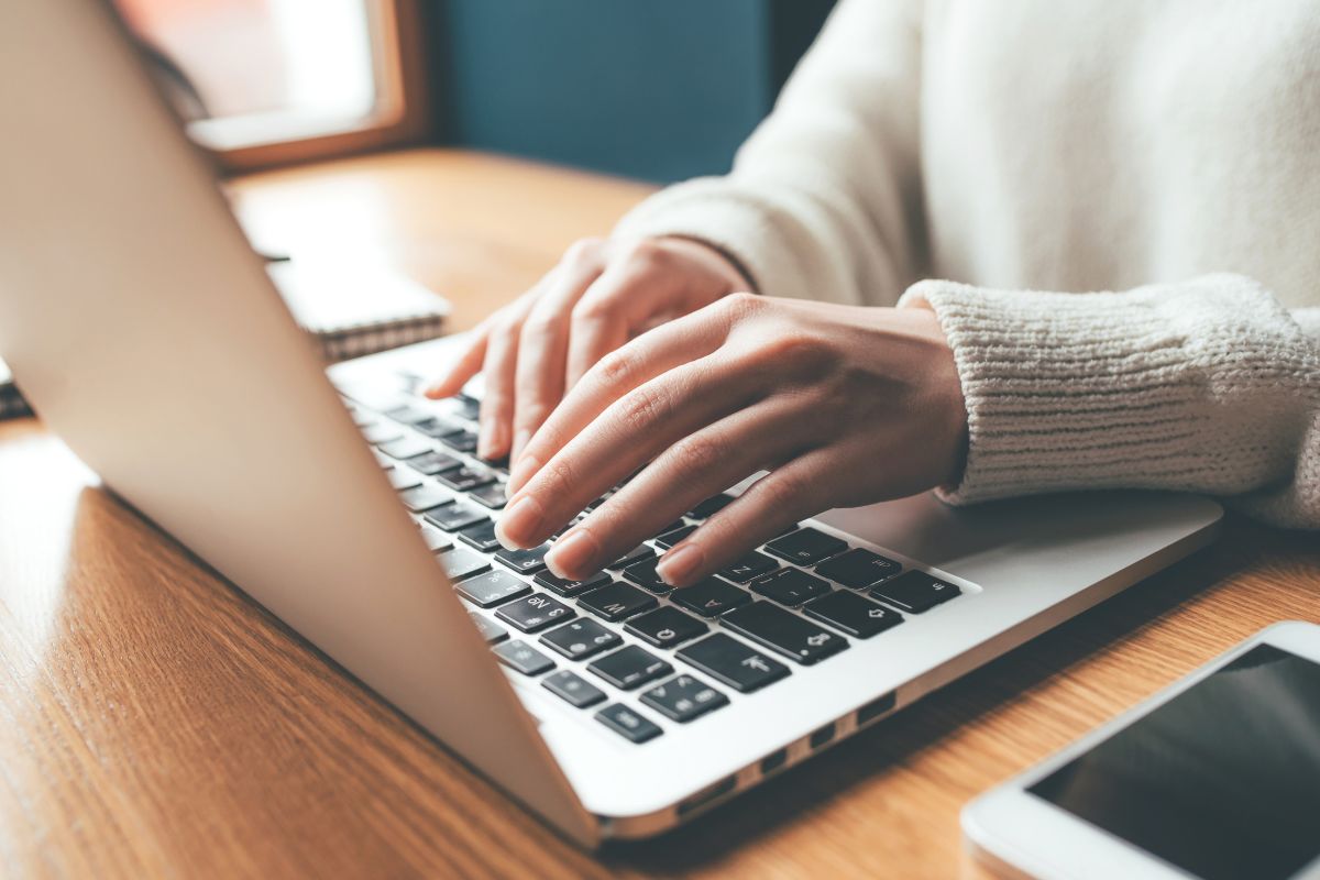 The image shows a woman's hand using a laptop for a debt tracker.