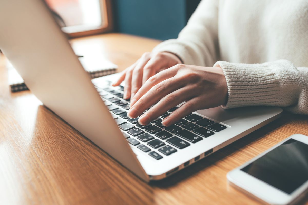 The photo shows a phone, a notebook, and a pen, and a girl's hand using a laptop referring to the use of visual habit trackers that help your brain stay focused.