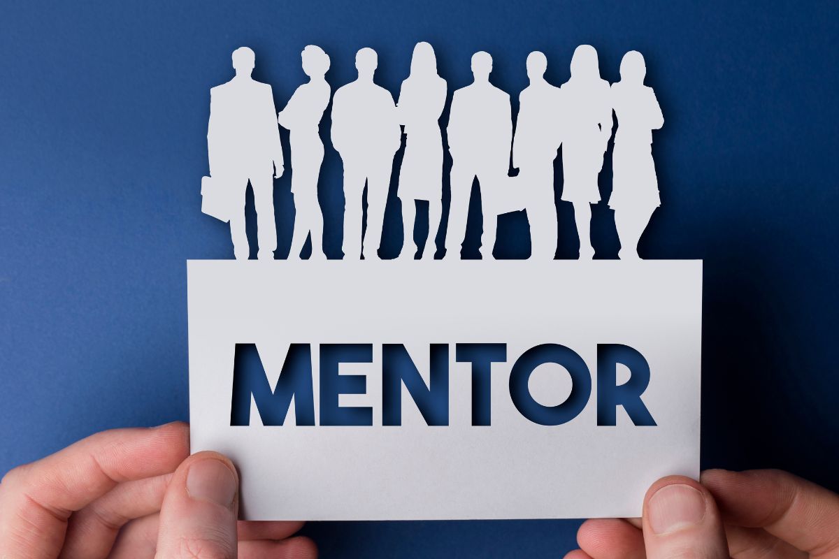 A man's hand holding cut paper with mentor wording.