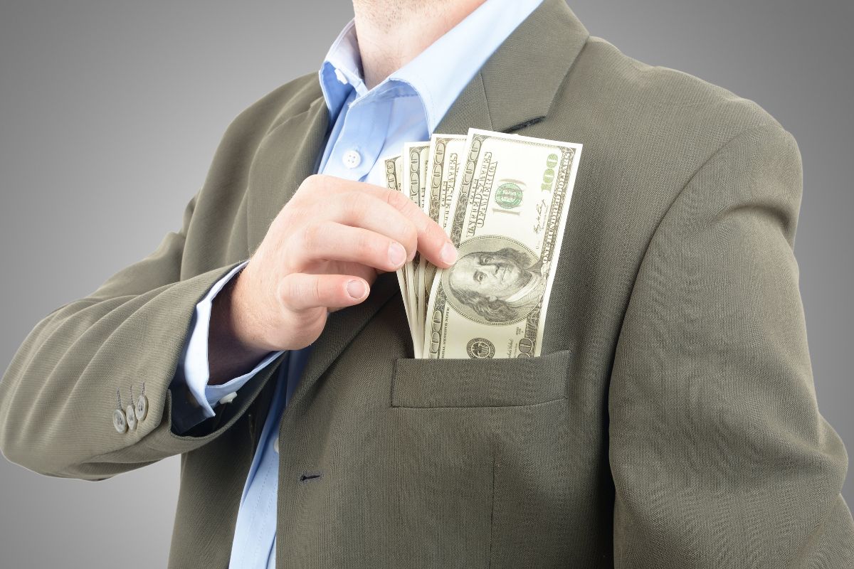 The picture shows a man in a suit showing off his money in a pocket referring to becoming independently wealthy with creative risks, small wins, and the right mindset.
