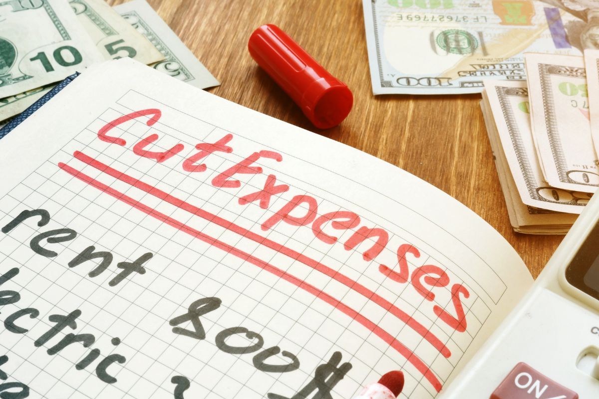 The photo shows dollar bills and a notebook with cut expenses wording.