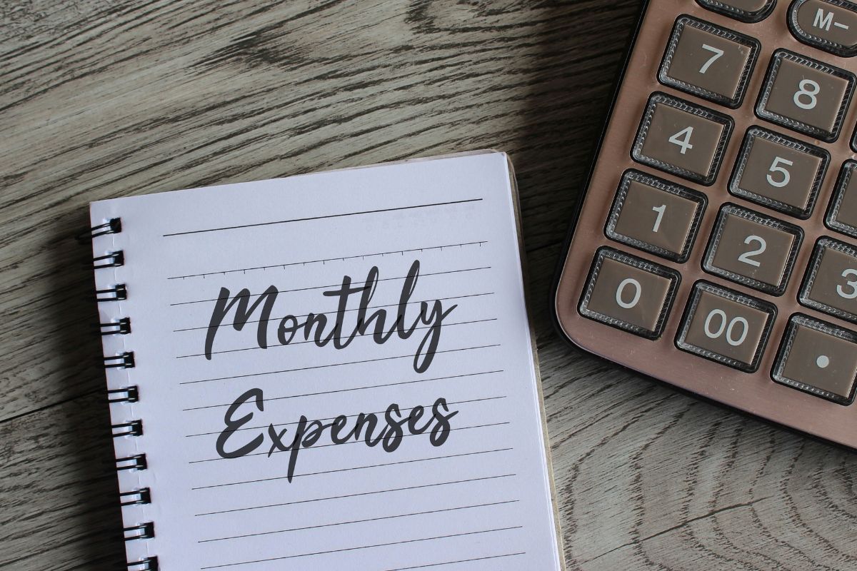 The photo shows a calculator and a notebook with monthly expenses.
