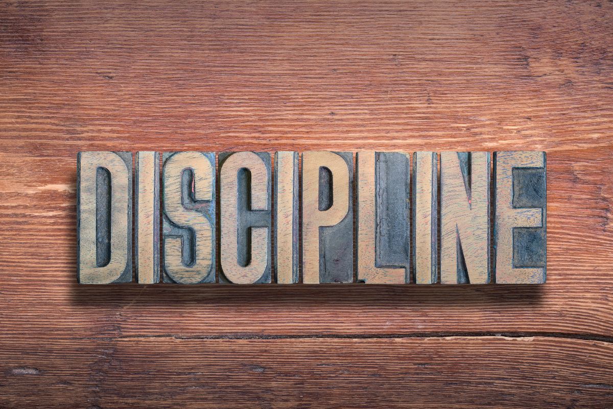 The image shows a wooden letter at the table which means staying disciplined and consistent which leads to financial changes.