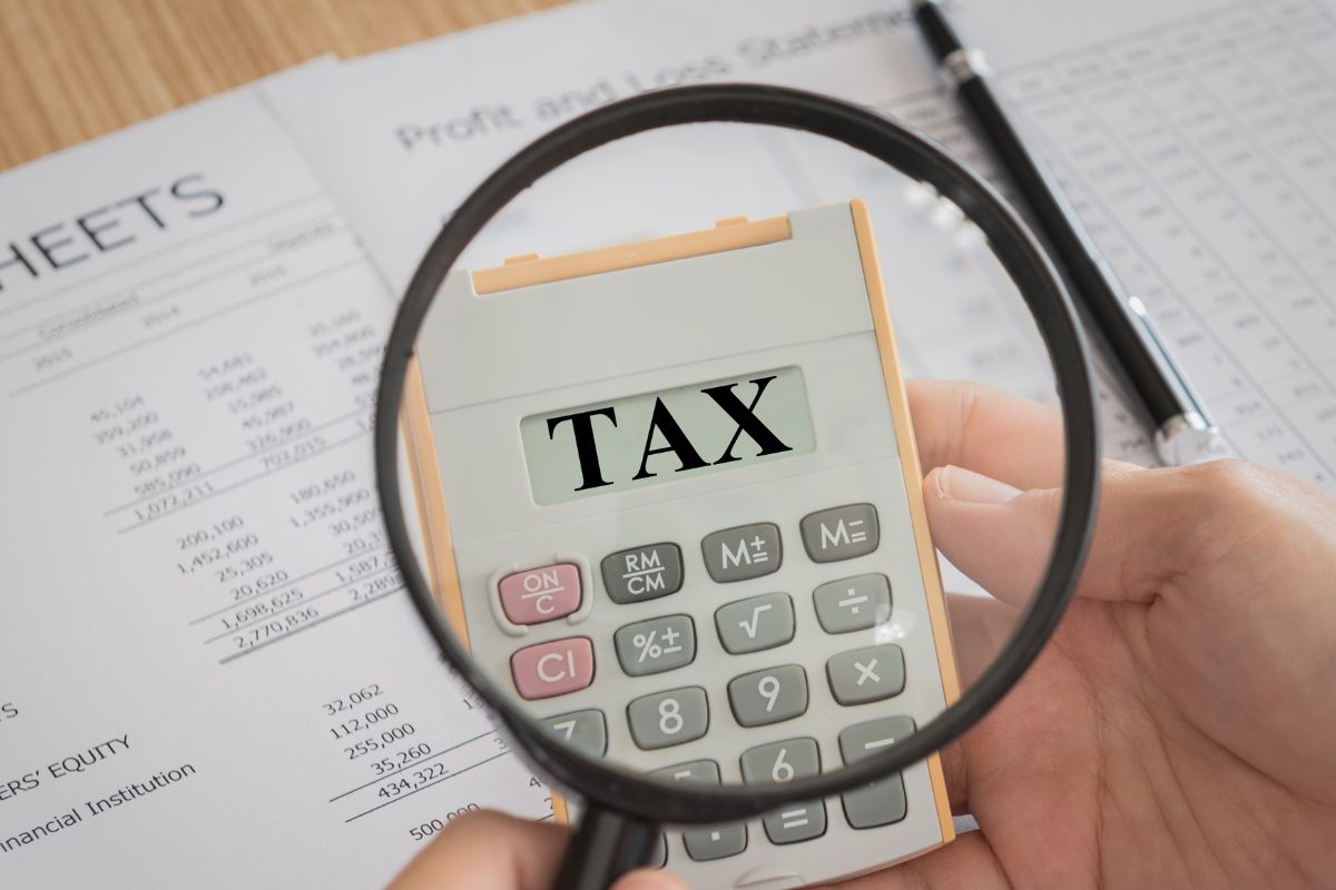 The image shows a man's hand holding a calculator with tax wording.