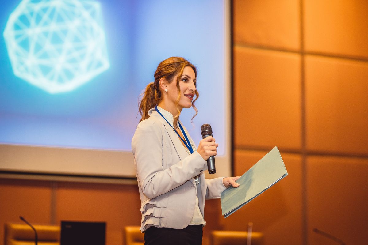 The photo shows a woman dong a public speaking.