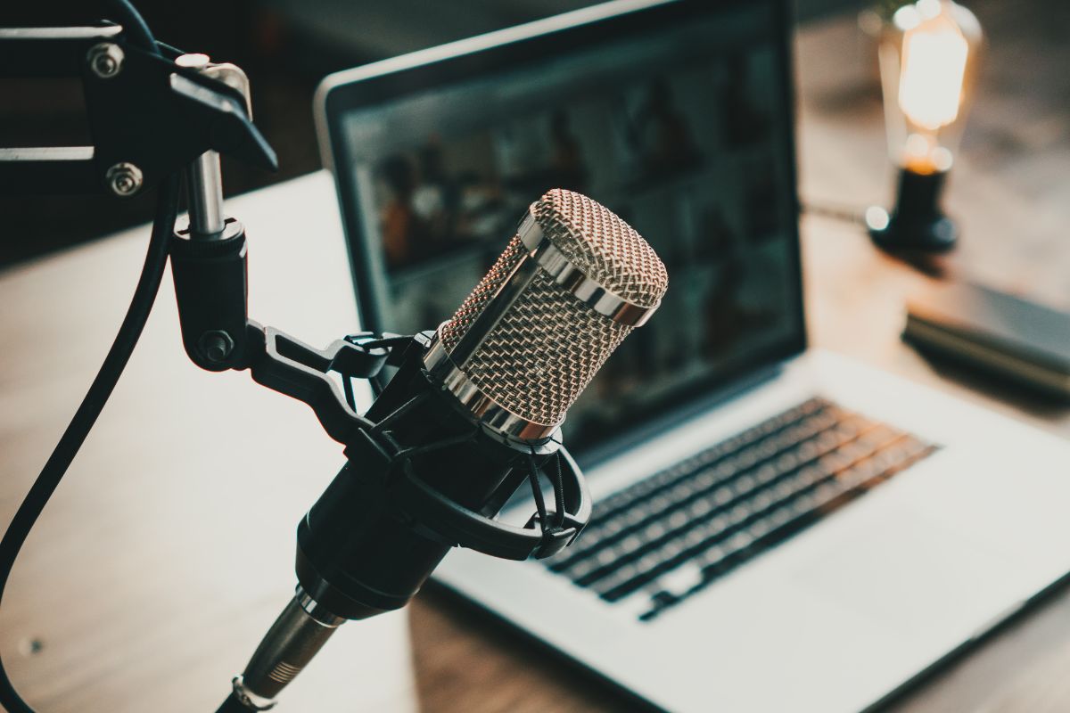 The image shows a laptop and a microphone for podcasting.