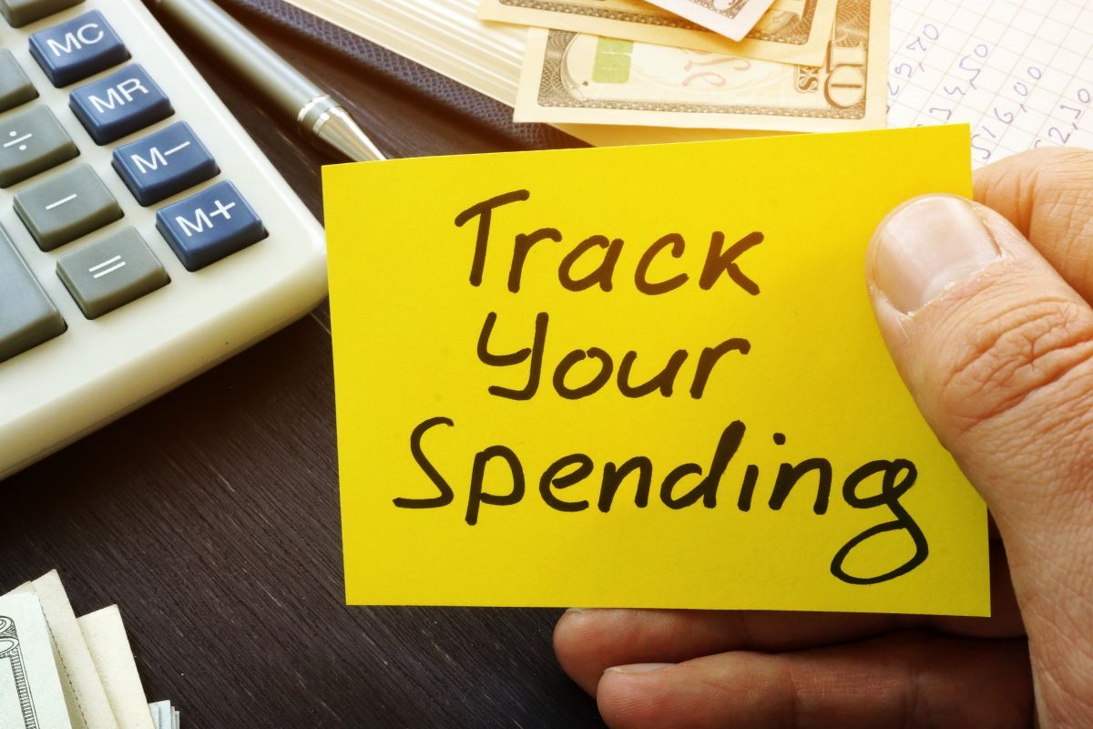 The image shows a man's hand and a paper with the Track Your Spending wording.