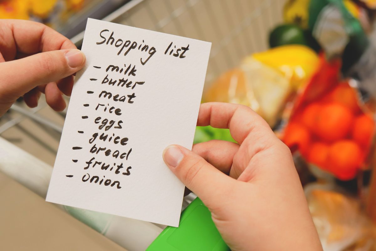 The image is about a woman's hand holding a paper with a shopping list.
