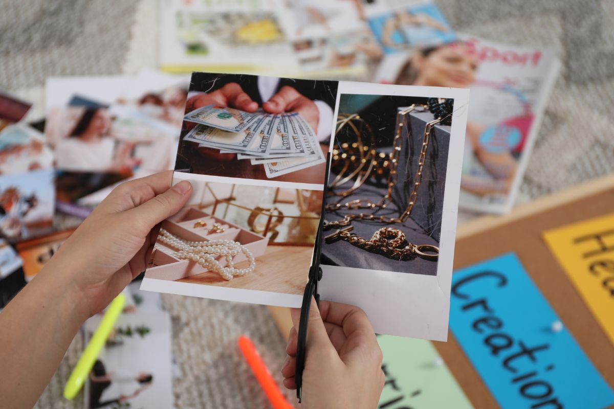 The photo shows a woman's hand creating a financial goal vision board.