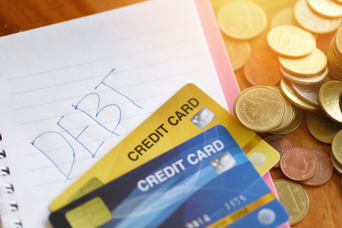 The image shows credit cards with debt wording on a notebook.