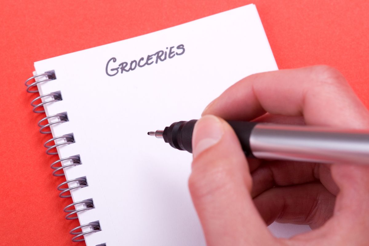 The picture shows a woman's hand and a notebook with grocery wording.