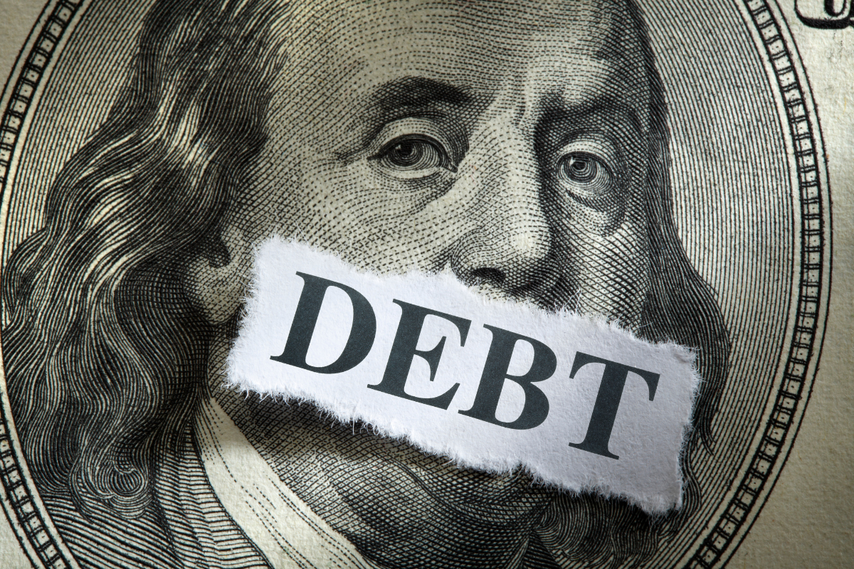 The picture is about a dollar bill and a paper with debt wording.
