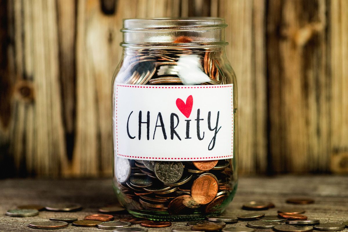 The image shows a jar filled with coins and a charity note.