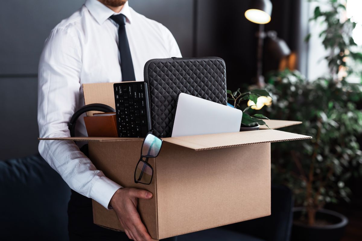 The picture shows a man holding a box of stuff after a job loss.