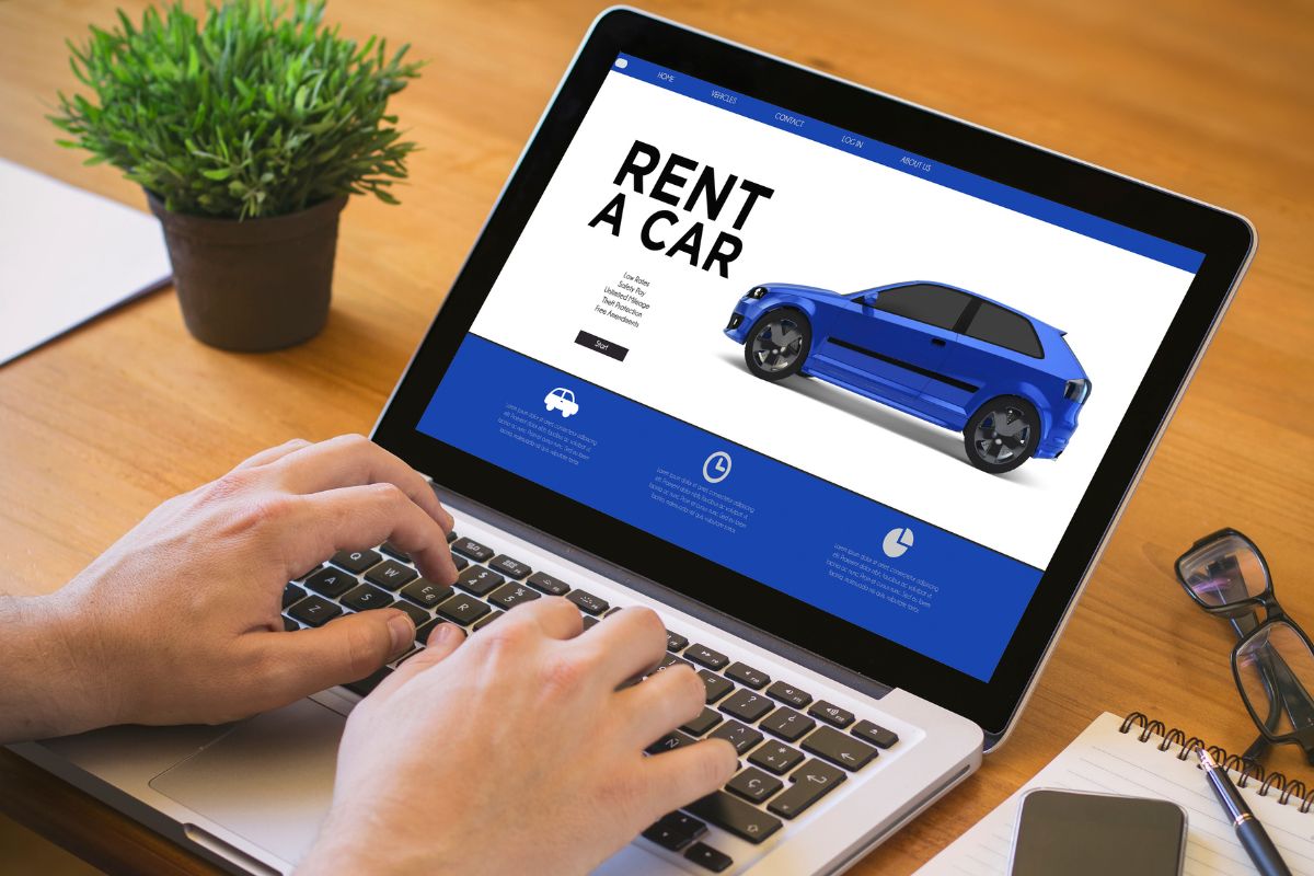 The photo shows a man's hand using a laptop to rent out his car.