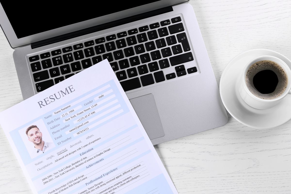 The picture shows a laptop and paper to offer resume writing.
