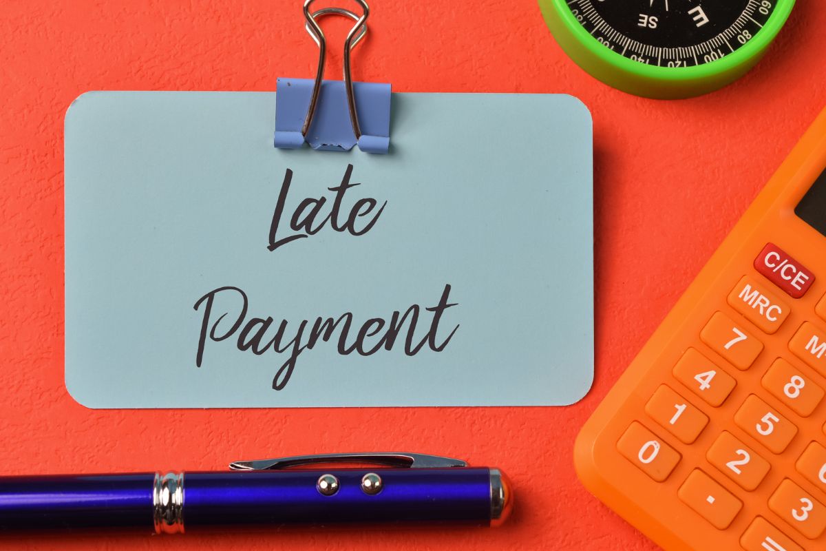 The image shows a calculator and a paper with late payment notes.