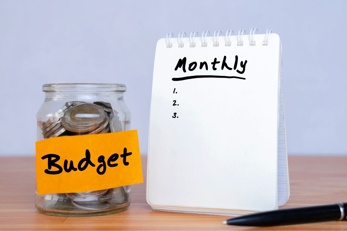 The image is about a jar with coins and a notebook with a monthly budget template.
