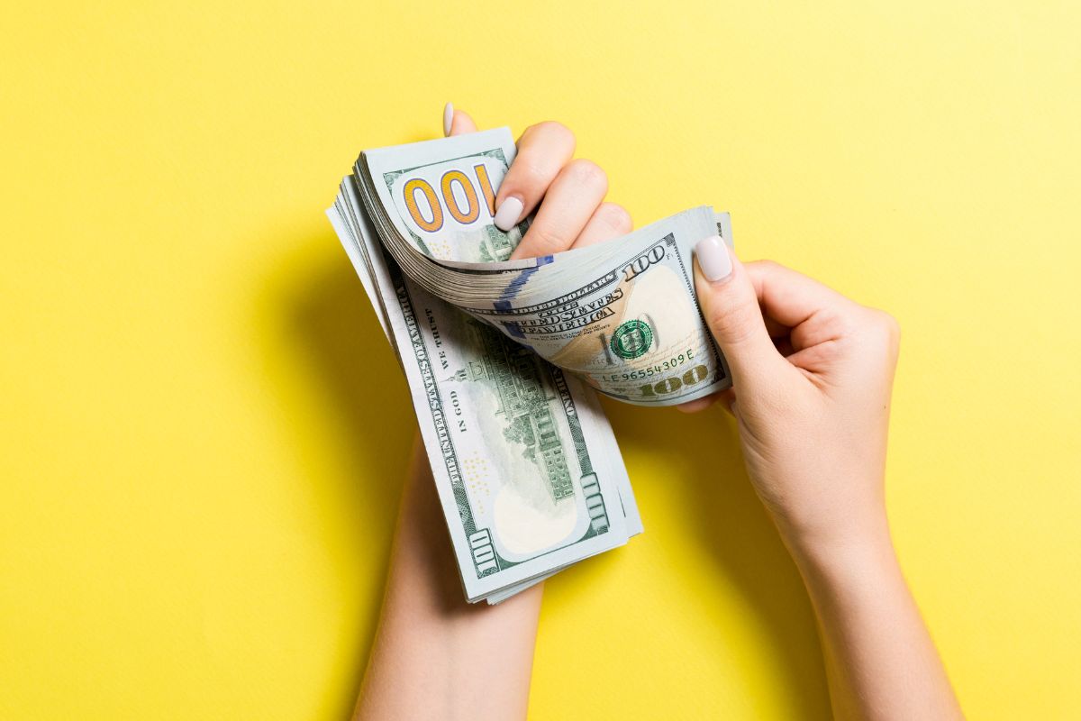 The image shows a lady's hand holding dollar bills to reset finances.