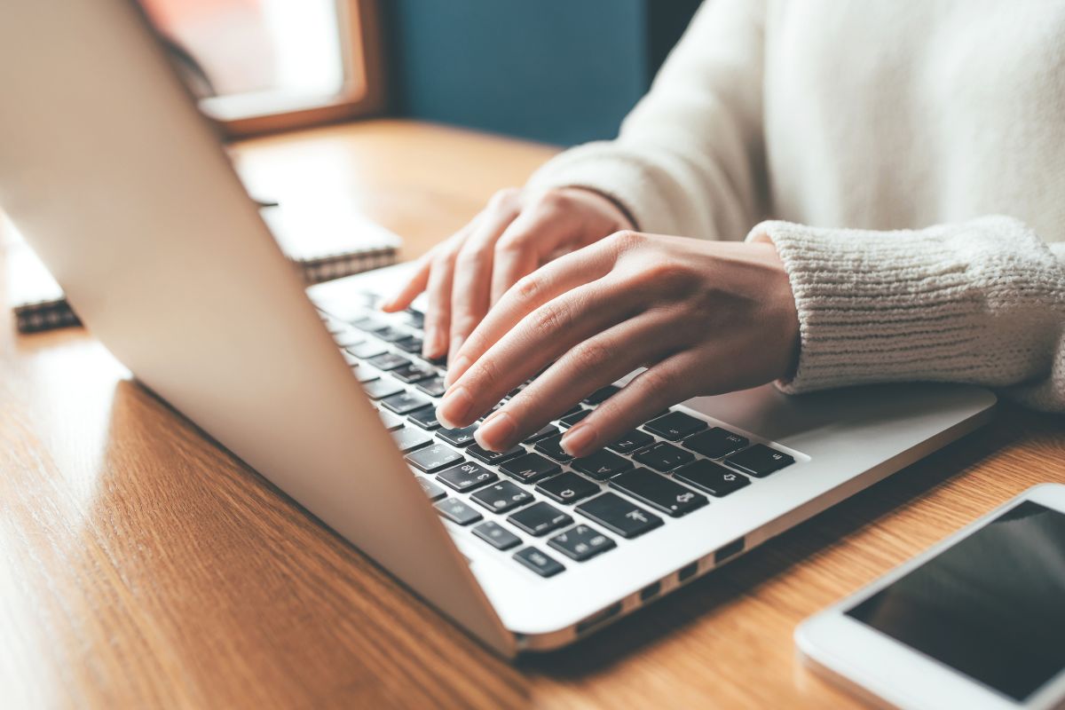 The picture shows a lady's hand typing on the laptop as an online chat agent.