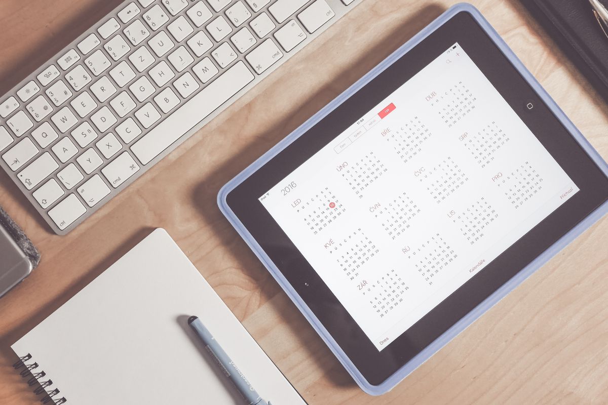 A picture of an iPad with a calendar, and a keyboard and a notebook.