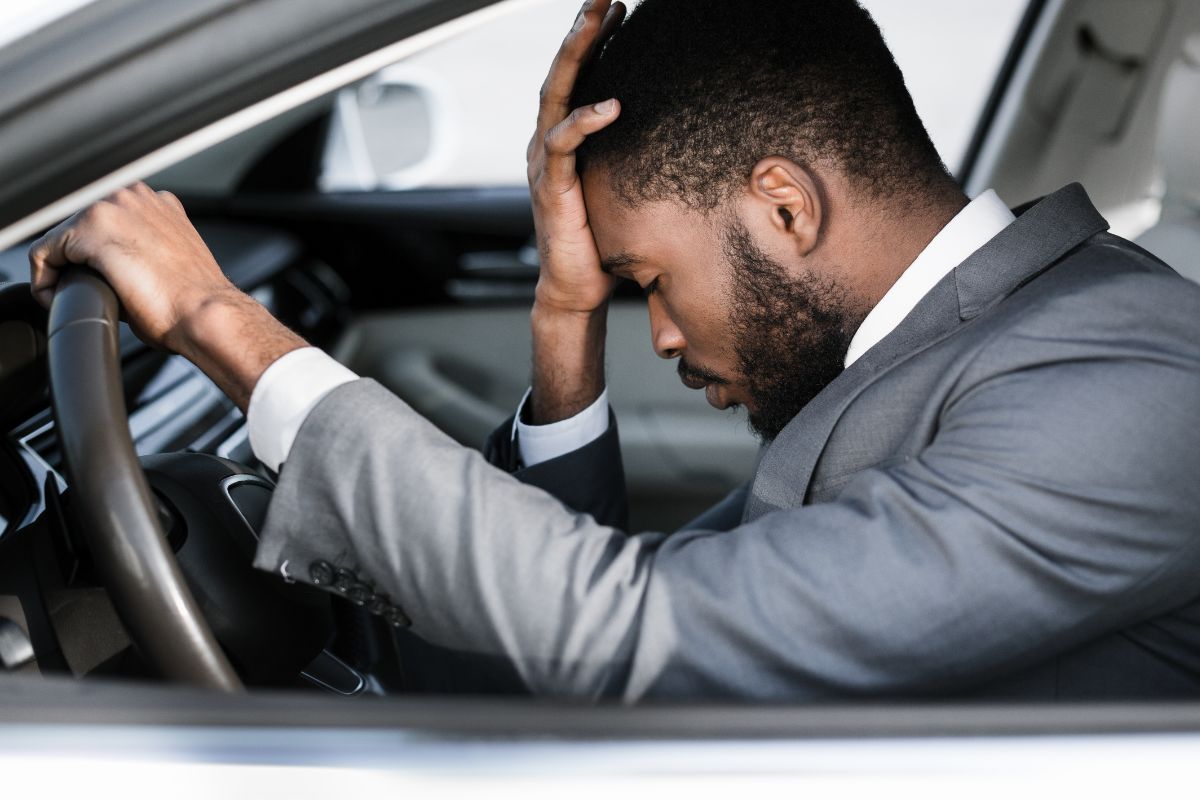 A picture of a man facepalming in his car. 