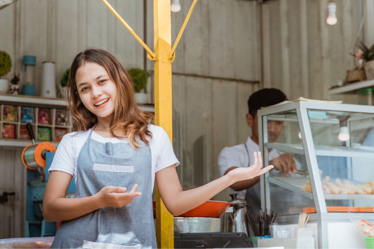 A picture of a lady selling foods at a market.