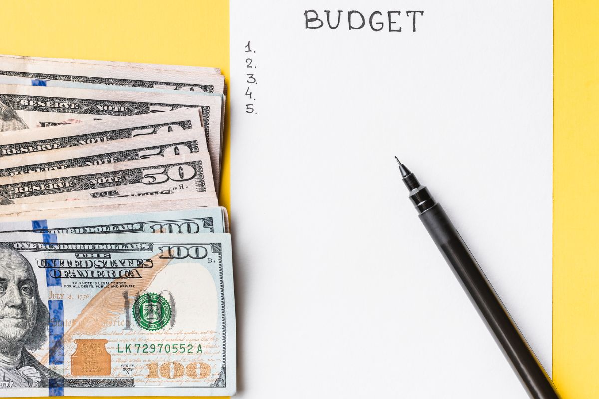 The picture is about dollar bills and a paper with budget list.