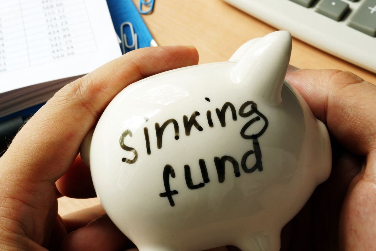 The image shows a man's hand holding a piggy bank with sinking fund wording.