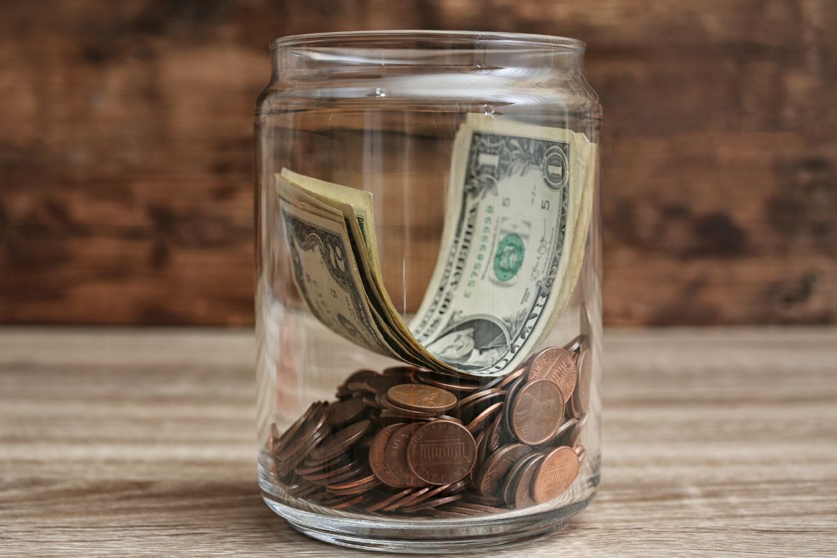 The image shows a jar filled with coins and dollar bills for the sinking fund.