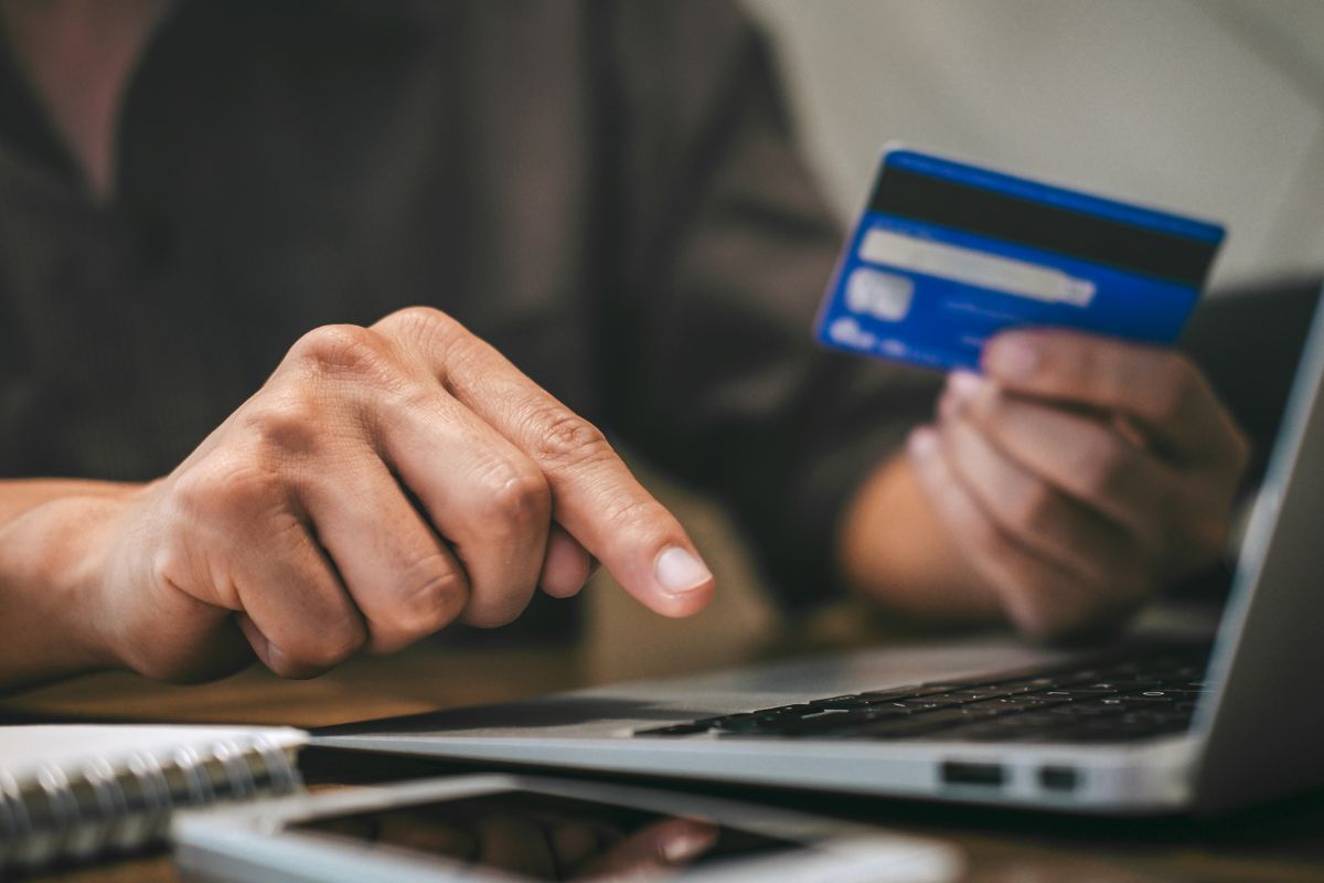 The picture shows a man's hand using a laptop to pay minimum on credit cards.