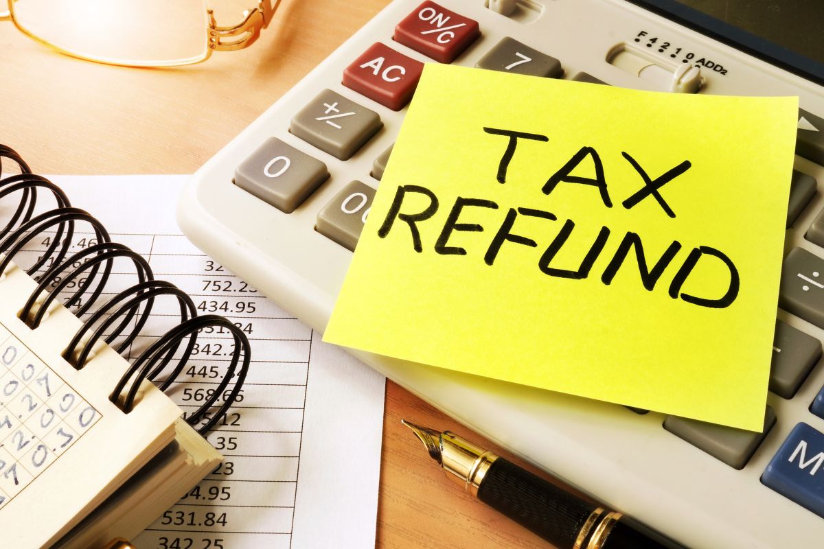 The image shows a calculator, a notebook, and a paper with a tax refund note. 