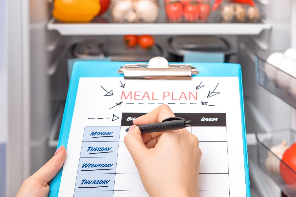 The photo shows a woman's hand creating a meal plan before shopping.