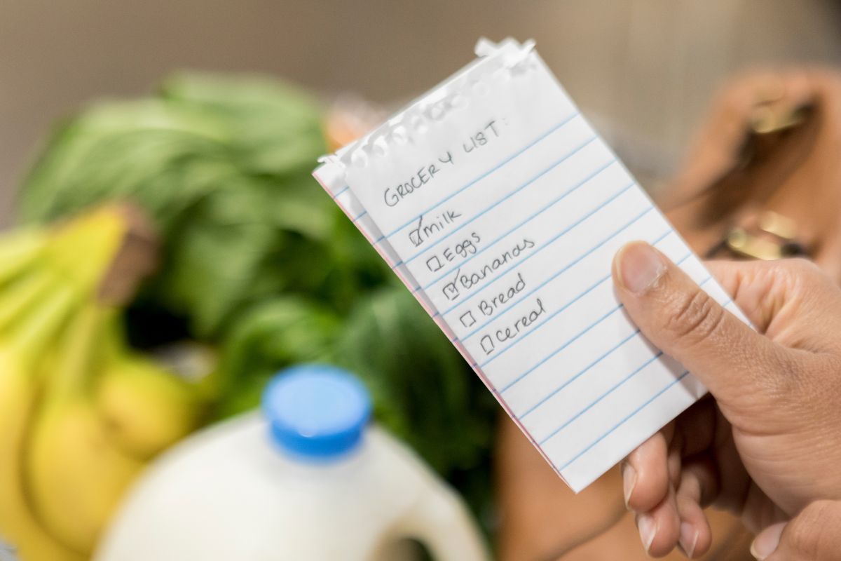 The image shows a woman's hand holding a paper of grocery list.