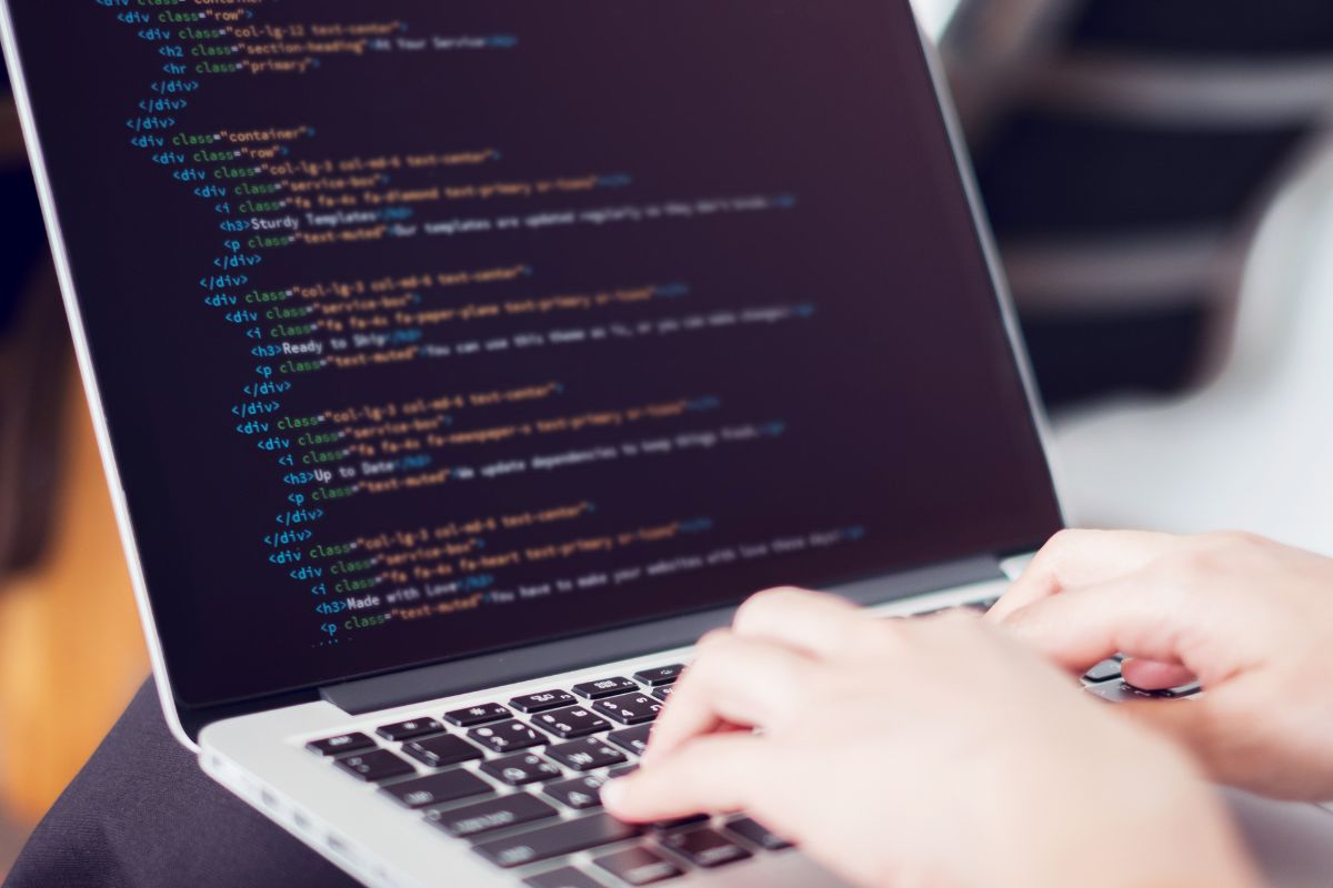 The photo shows a woman's hand working on a laptop in web development.
