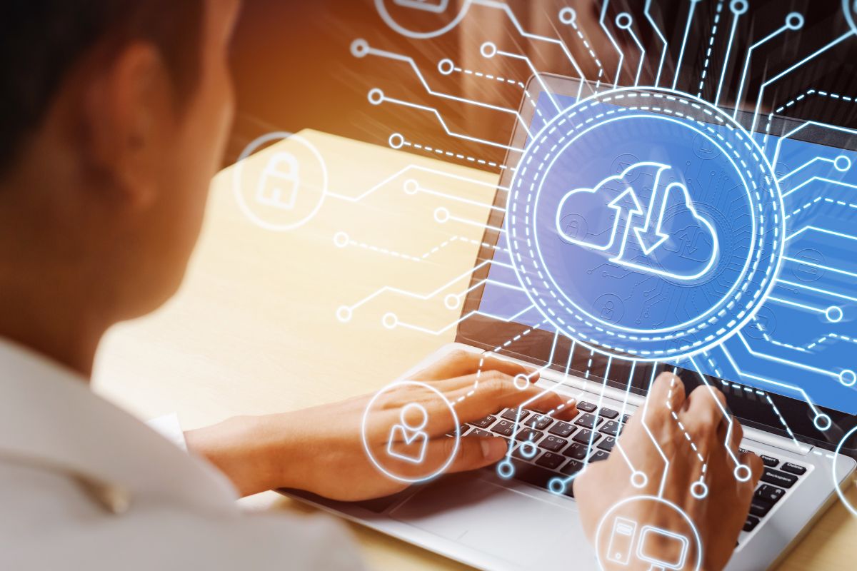 The picture shows a man's hand using a laptop for cloud computing work.