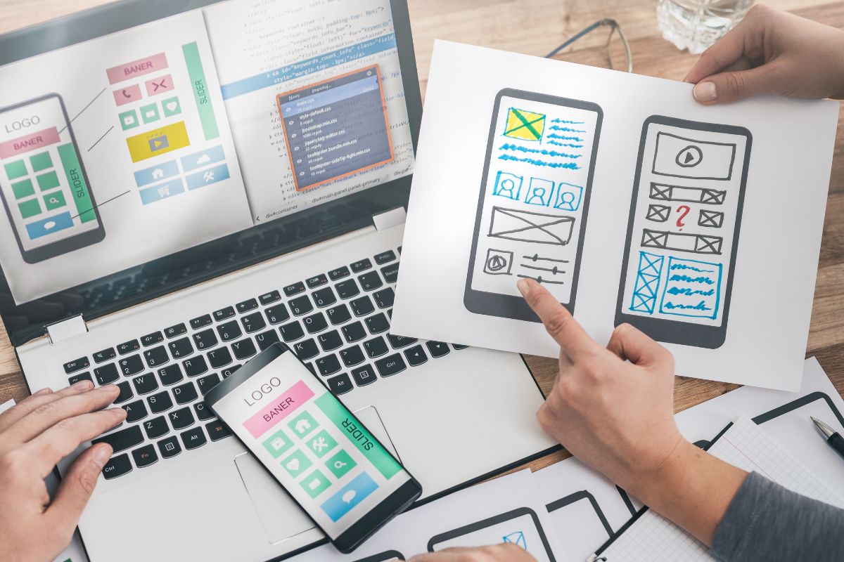 The image shows a laptop and men working on a mobile app development.