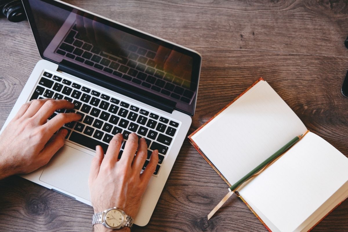 The picture is about a notebook and a man's hand working on technical writing.
