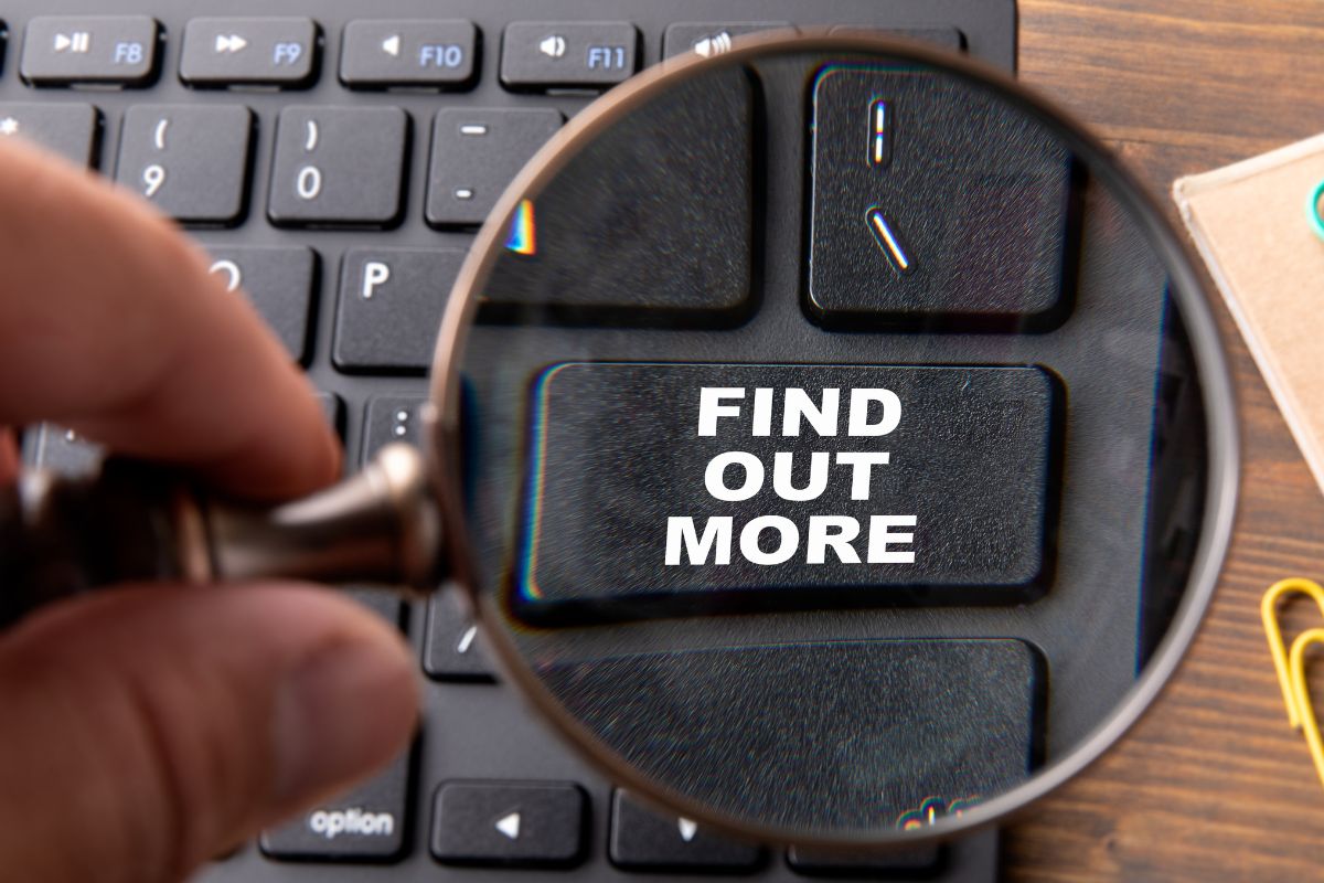 The image shows a man's hand using a magnifying glass to focus on the word find out more.