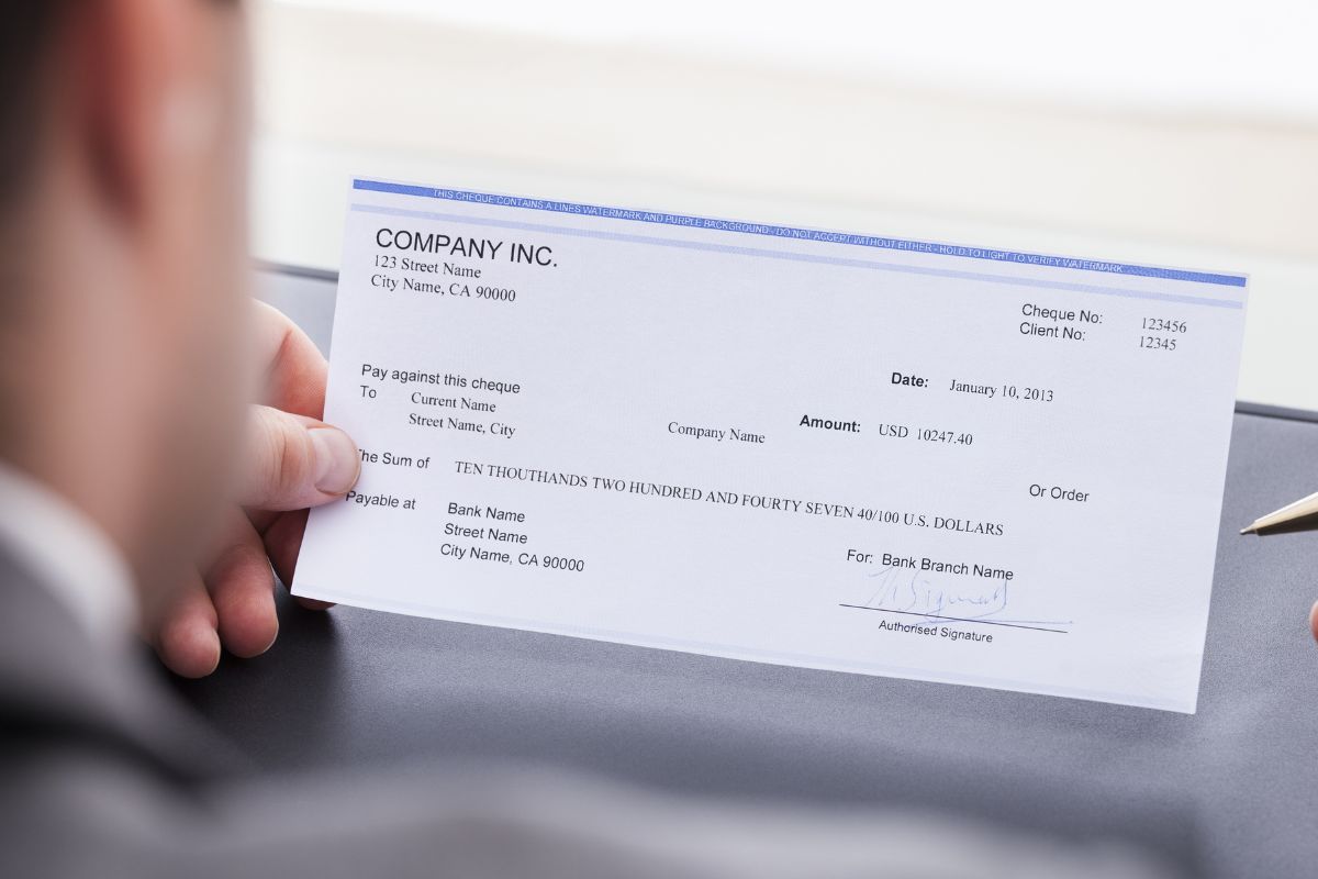 The photo shows a man holding a piece of paper and a pen which means paycheck to paycheck vs investing extra money is about building safety instead of just getting by.