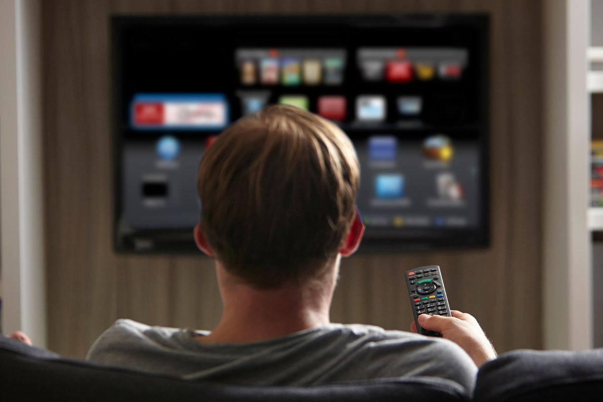 The image shows a man's hand holding a remote control indicating that watches TV for hours