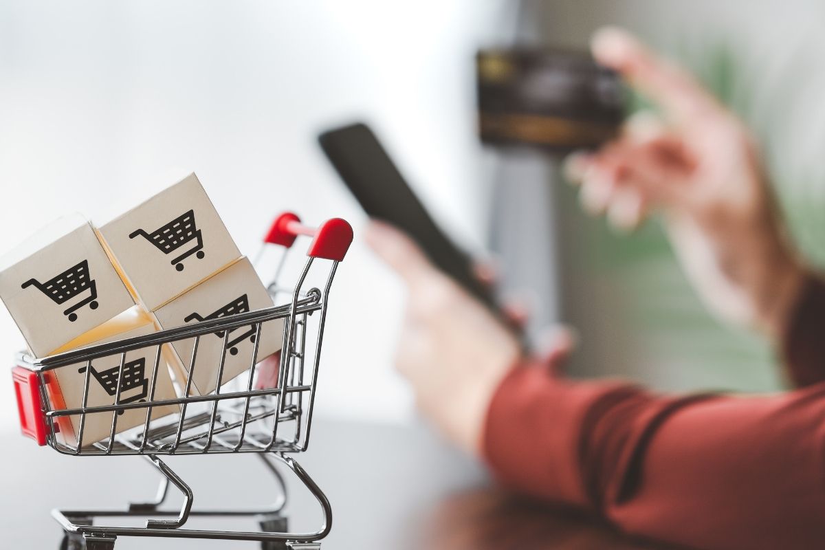 The photo tells about a cart and icons and a man's hand holding a card and phone referring to buys now vs waits plans