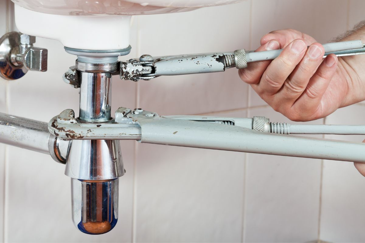 The photo tells about a man's hand repairing the plumbing.