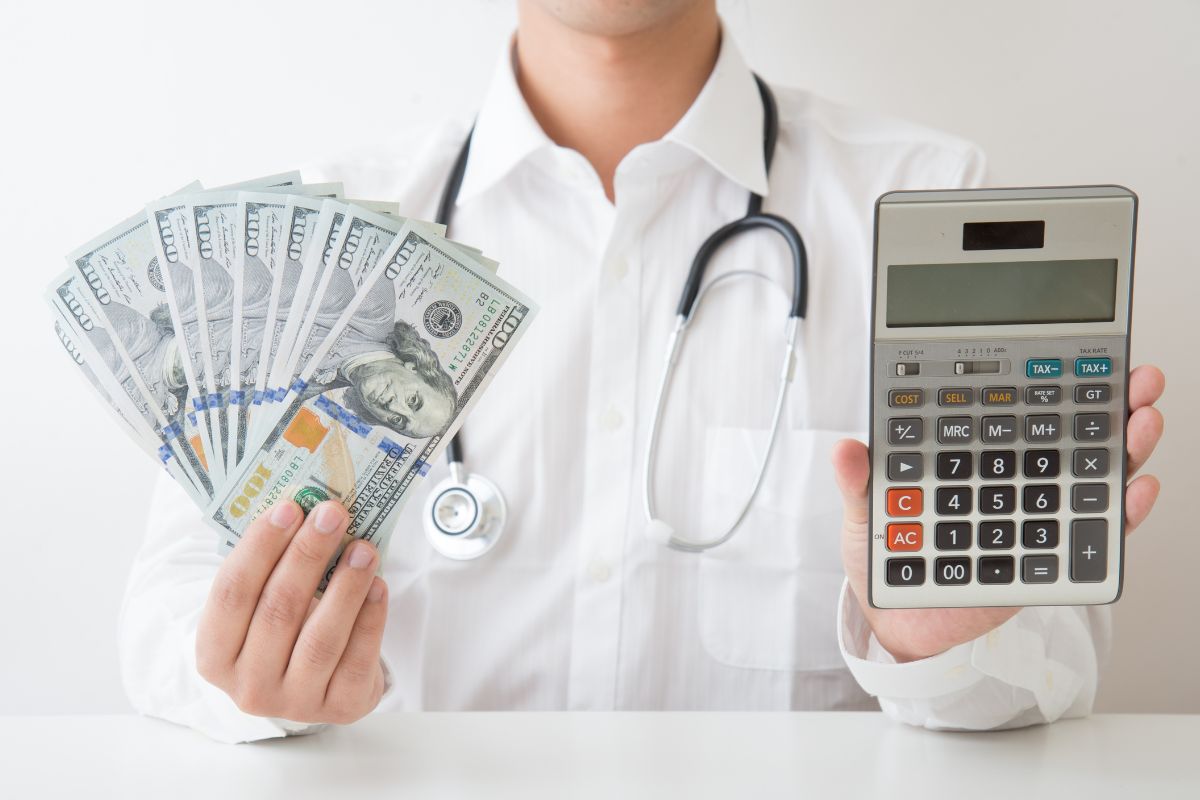 The photo of a doctor holding dollar bills and a calculator for medical expenses.