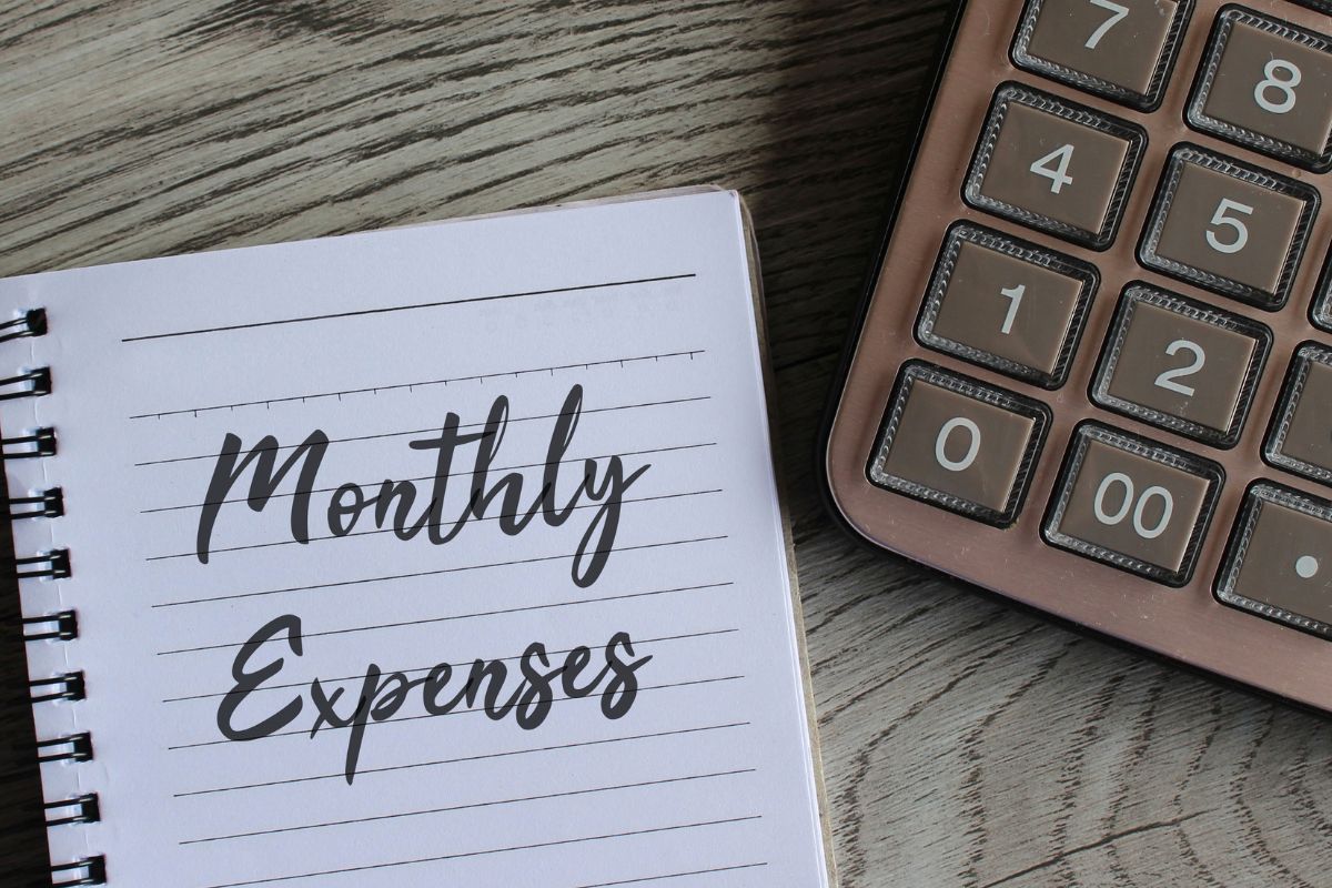 The photo shows a calculator and a notebook with monthly expenses wording.