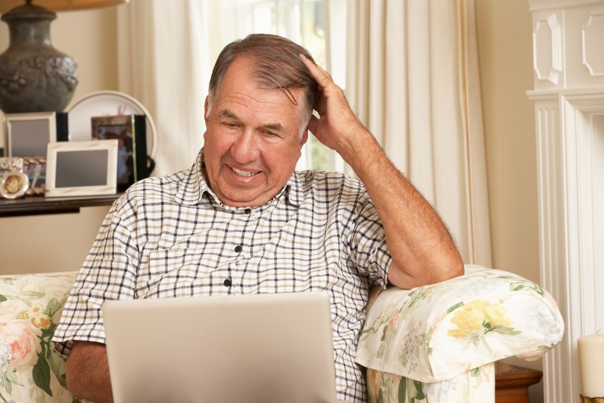 The image shows a frustrated senior man using a laptop.