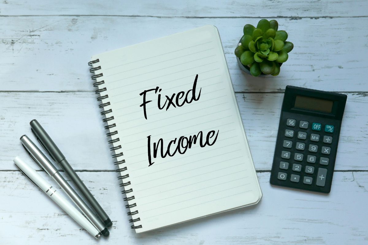 The picture of a calculator, pens, a plant, and a notebook with fixed income wordings.
