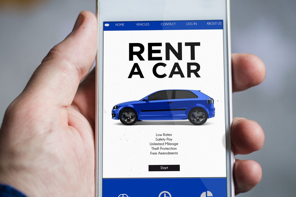 The photo shows a man's hand holding a phone with rent a car screen display.
