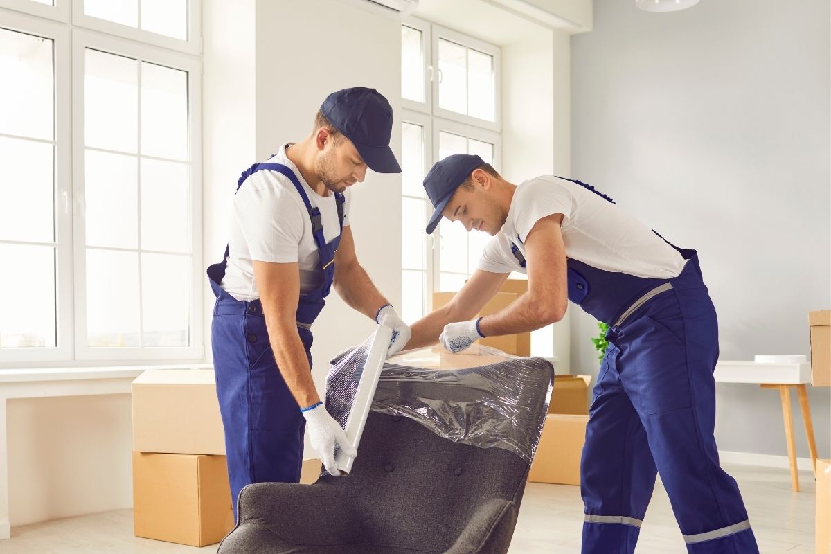The picture of moving service workers wrapping a chair with plastic wrappers.